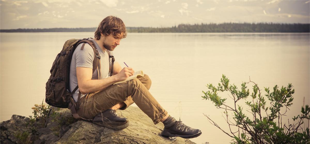 Man writing in a notebook in front of a lake