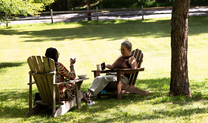 Two women in Adirondack chairs chat under a tree