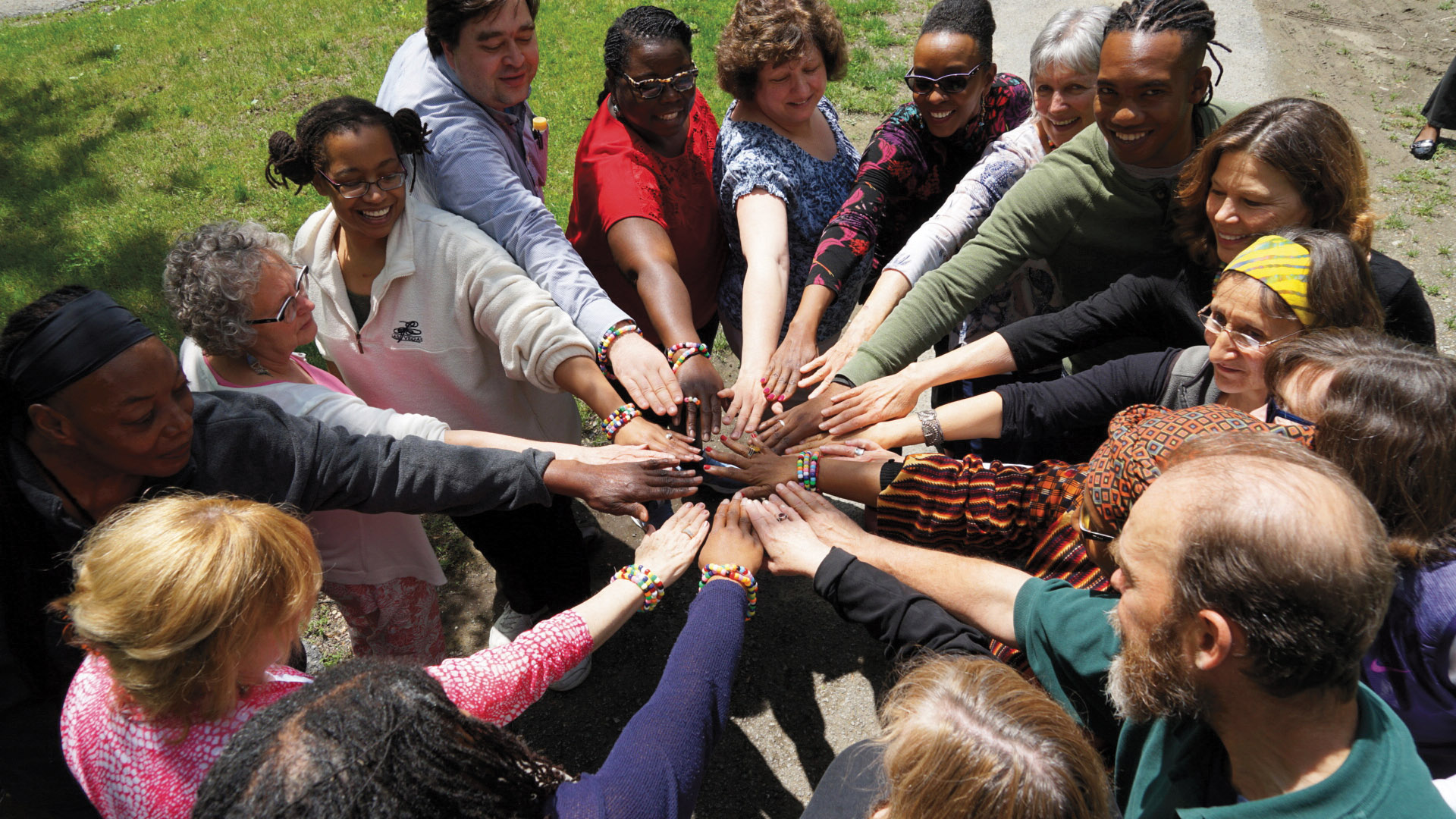 A group of diverse individuals standing in a circle putting their hands together in community.