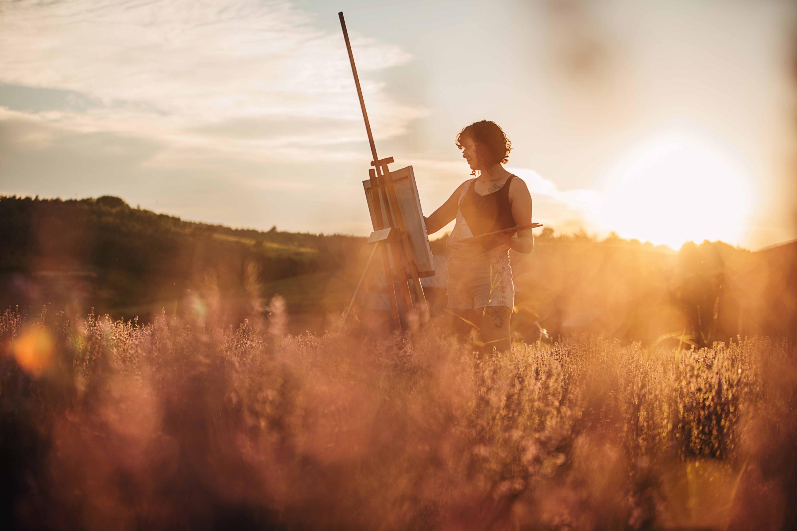 Woman paintis at a easel in a field at dawn