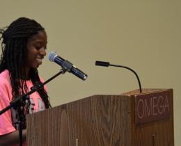 Young woman delivering a compelling speech at a podium, using confident body language and a smile—an example of powerful storytelling techniques in action.
