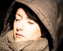 Woman in winter coat and scarf standing in sunlight with eyes closed, symbolizing peacefulness and holistic self-care for seasonal depression (SAD).