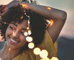 Joyful woman holding glowing fairy lights at sunset, symbolizing the radiant energy, intuition, and higher purpose of a lightworker.
