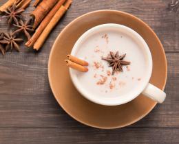 Cup of warm spiced milk with cinnamon and star anise on a wooden table, illustrating Ayurvedic winter diet tips for warmth and digestion.