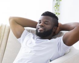 A relaxed man with closed eyes resting on a couch, illustrating calmness and relaxation as part of exercises to help you fall asleep with ease.