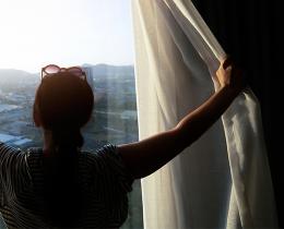 Woman opening bedroom curtains to welcome morning sunlight, symbolizing a peaceful morning routine and mindfulness ritual for starting a calm and centered day.