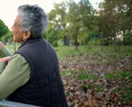 Two people smiling and clinking mugs together on a park bench, symbolizing friendship, connection, and practices that alleviate loneliness.