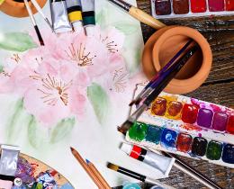 Artist workspace with watercolor painting, brushes, palettes, and art supplies for creative practice.