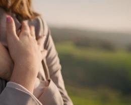 Woman embracing herself outdoors in soft sunlight, symbolizing self-compassion, healing, and recovery from heartbreak.