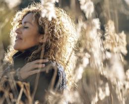 Woman with eyes closed peacefully standing in sunlit tall grass, embracing mindfulness, self-acceptance, and inner peace in nature.