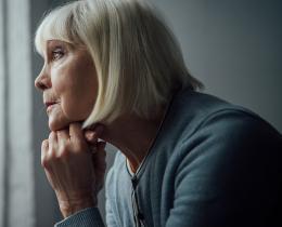 Close-up of woman resting chin on hands, staring out window in contemplation and emotional grief