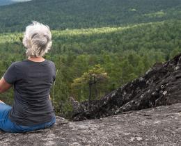 Person meditating on a rocky overlook above forest to reconnect with creativity and nature.