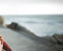 Woman wrapped in a blanket gazing toward the ocean, symbolizing calm, emotional resilience, and healing through Presence Psychotherapy.