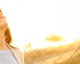 Woman standing outdoors with eyes closed in sunlight, symbolizing calm breathing and nervous system regulation through daily rhythm.