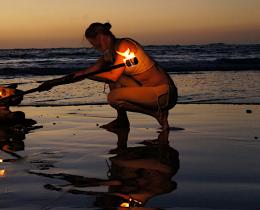 Woman tending a beach bonfire at sunset, reflecting the power of nature-based rituals and sacred traditions during a retreat for regeneration and spiritual renewal.