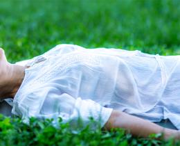 Woman resting outdoors on a mat in grass, representing deep sleep, relaxation, and restorative practice.