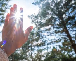 Person reaching towards the sun, with the light filtering through their fingers, symbolizing a connection with spirituality.