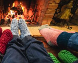 Cozy sock-covered feet gathered by a warm fire, symbolizing comfort and connection as winter days grow shorter.