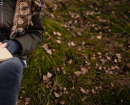 Person writing in a journal outdoors during a symbolizing memoir writing and creative storytelling