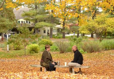 2 people conversing on bench surrounded by autumn leaves