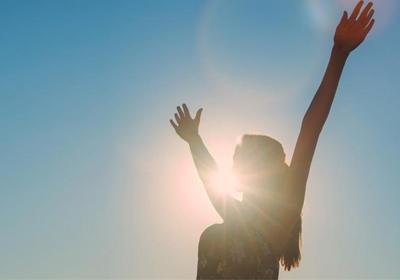 Woman with hands up with bright sun behind