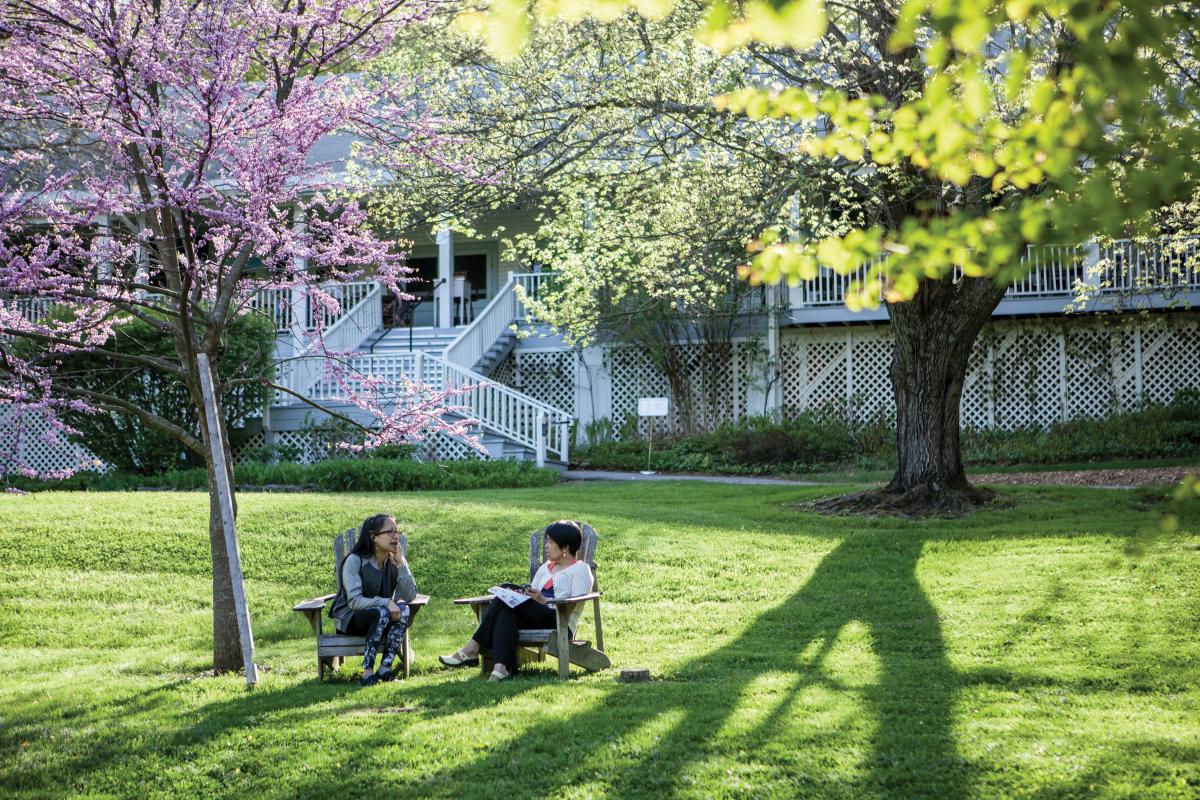 2 people sitting in Adirondack chairs under flowering spring trees