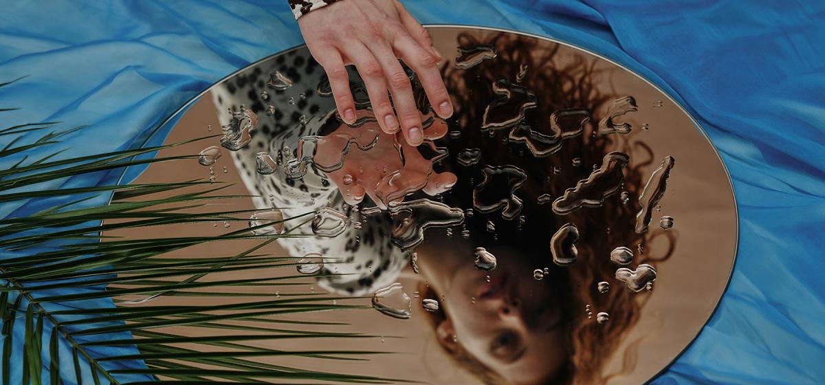Person touching their reflection in a mirror covered in water, symbolizing reconnecting with their self