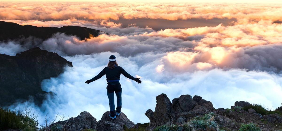 Woman standing above the fog on a rocky ledge