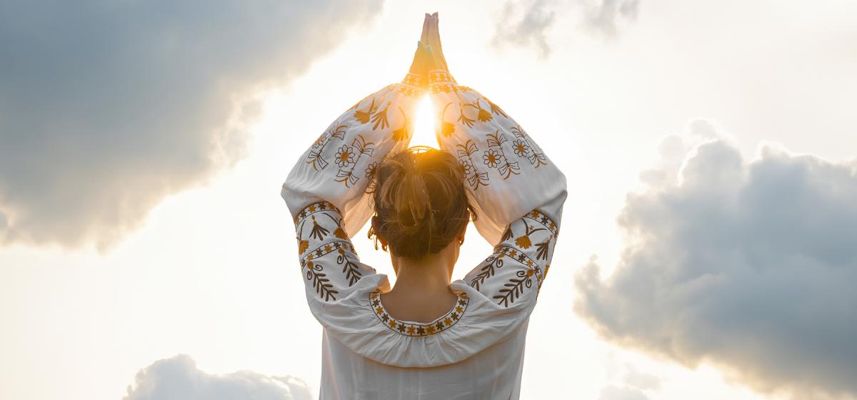 Person with hands in prayer position near the sun