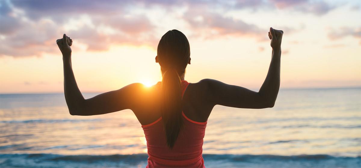 Woman flexing muscles at sunset
