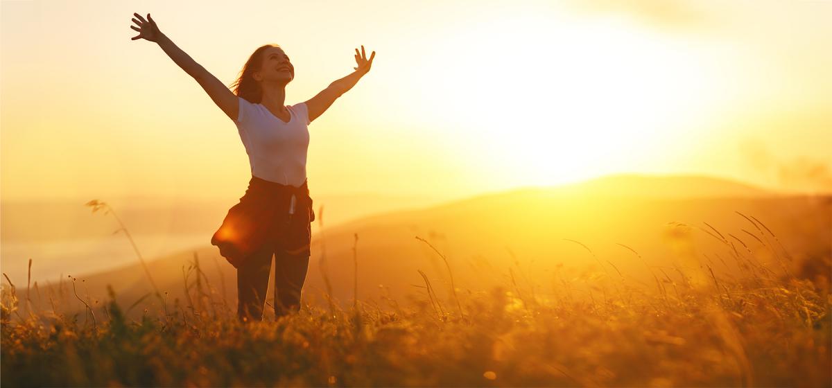 Person standing with arms open at sunset