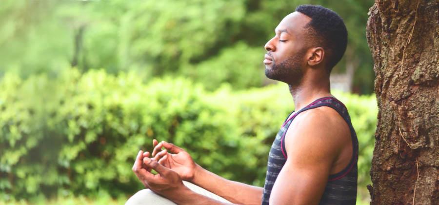 Man meditating outside next to a tree
