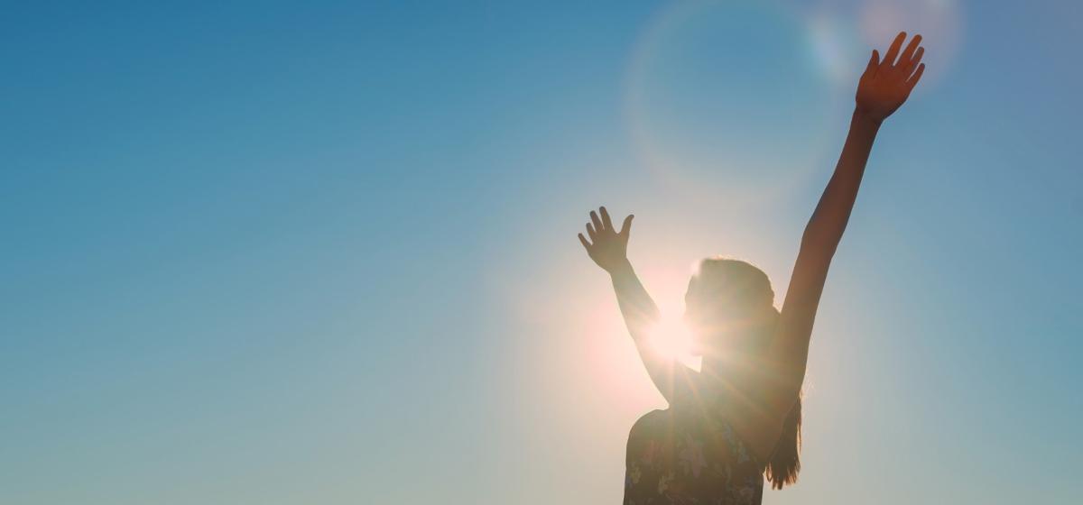 Woman with hands raised in the air in front of sun