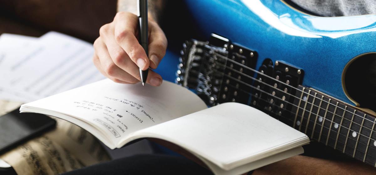 Person writing a song with notebook and electric guitar