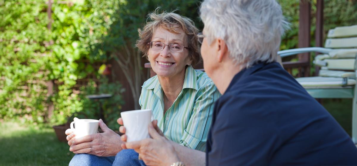 Two grandmothers enjoying a cup of tea together outside