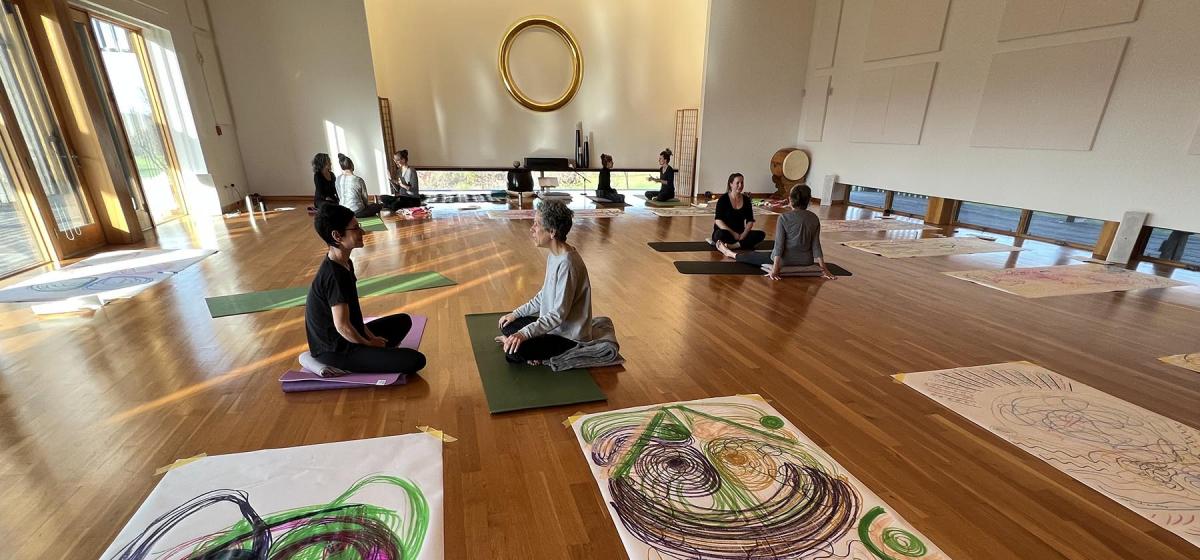 Group of people meditating in a room filled with large drawings