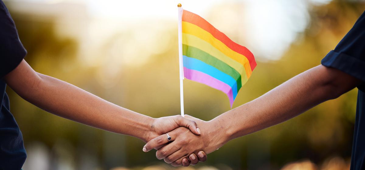 Two people holding hands with a rainbow flag in their hands