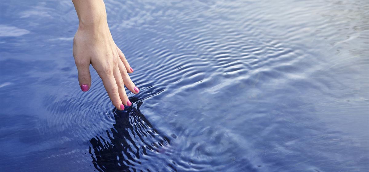Hand touching the water and leaving a ripple