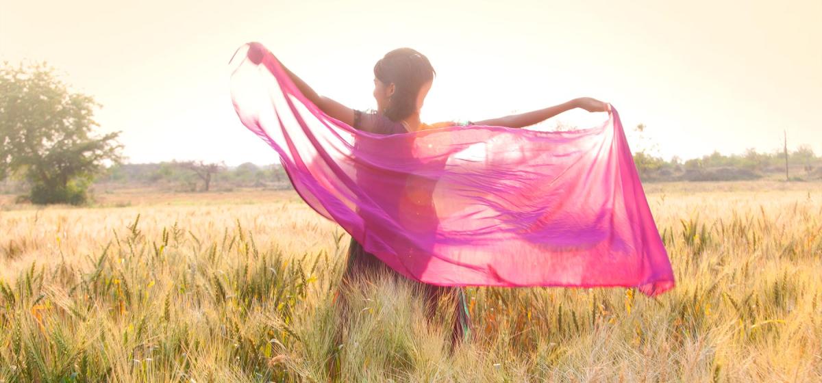 Woman standing joyfully in field, waving silky pink shawl in the wind