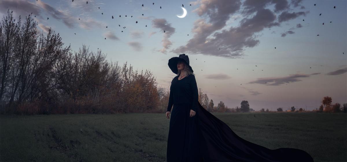 Witch standing in a field under the moon