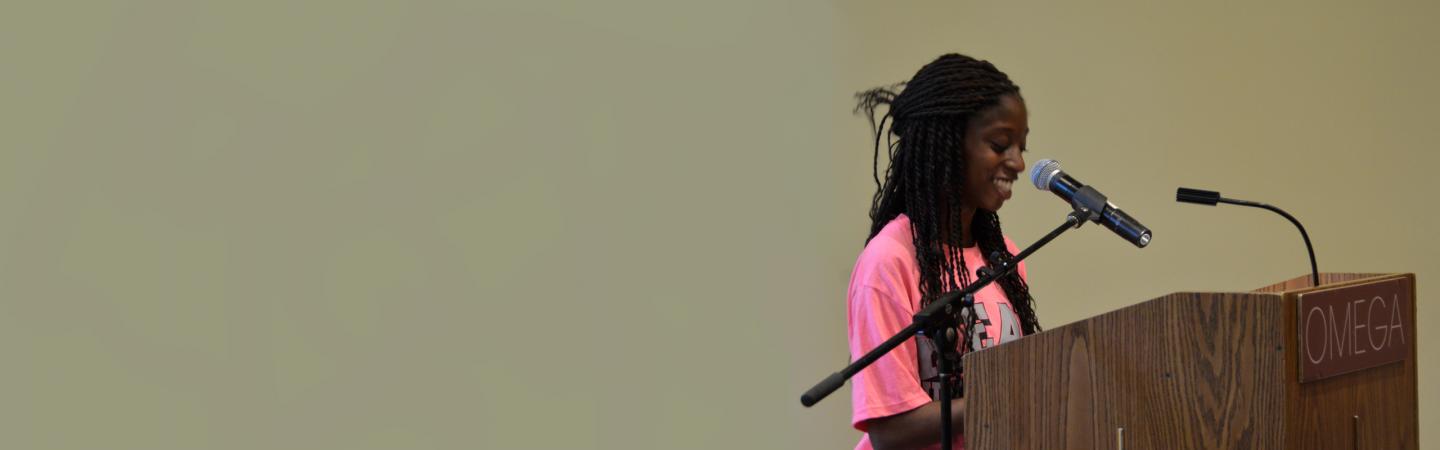Young woman delivering a compelling speech at a podium, using confident body language and a smile—an example of powerful storytelling techniques in action.