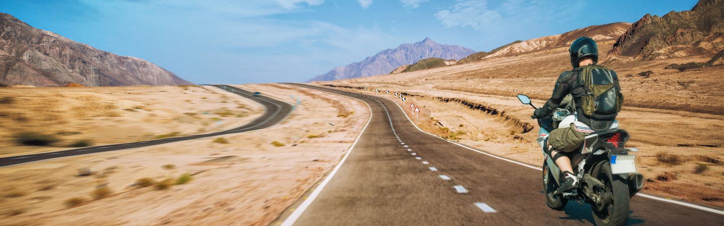 Motorcyclist riding through a vast desert landscape toward distant mountains, symbolizing the soul’s journey and exploration of the afterlife in mediumship beliefs.