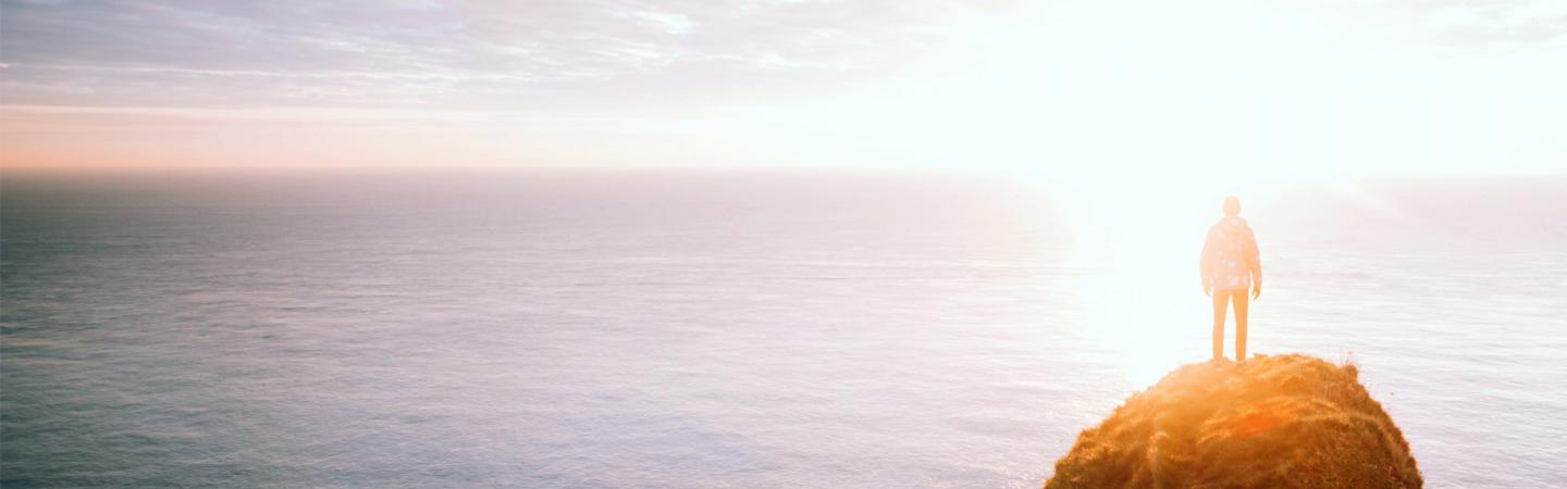 Person standing on cliff overlooking ocean at sunrise, symbolizing spiritual awakening and access to the Akashic Records as described by Edgar Cayce.