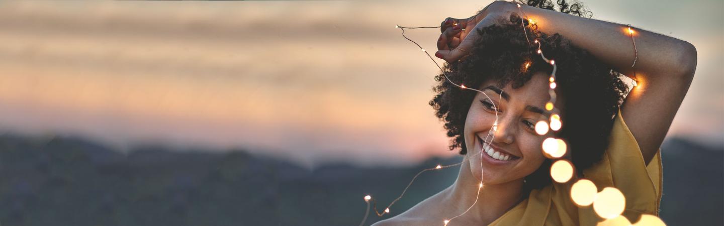 Joyful woman holding glowing fairy lights at sunset, symbolizing the radiant energy, intuition, and higher purpose of a lightworker.