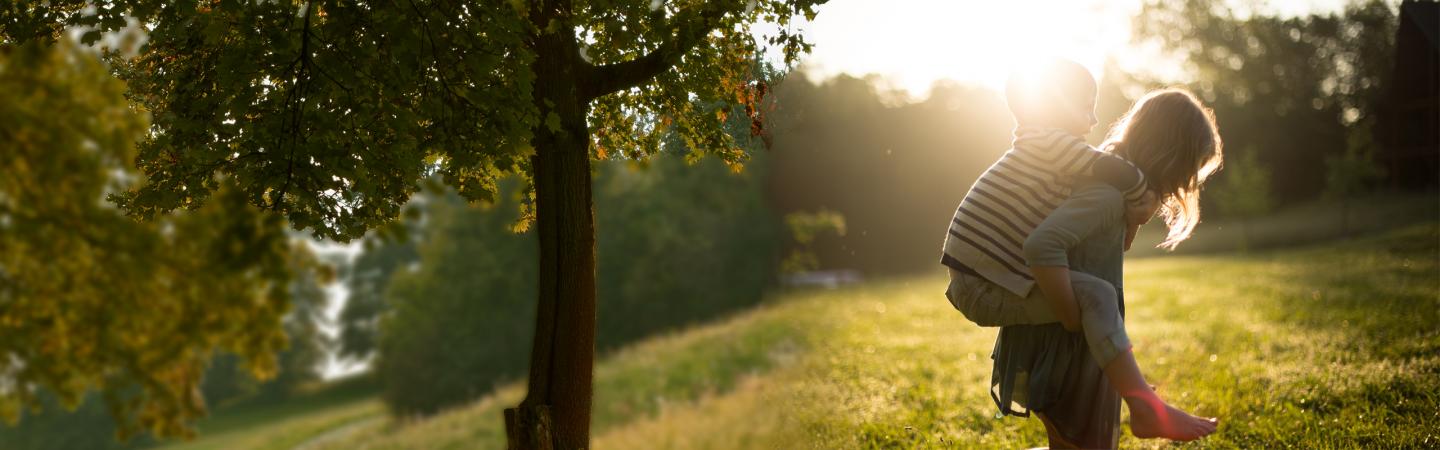 Parent carrying child through grassy field, emphasizing outdoor tick exposure and Lyme disease health risks.