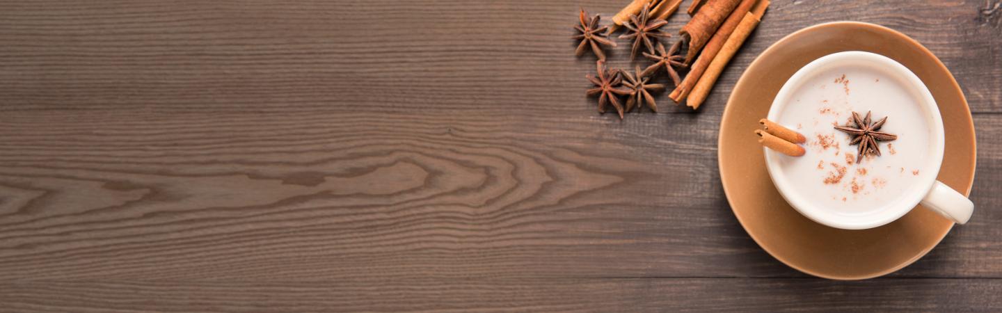 Cup of warm spiced milk with cinnamon and star anise on a wooden table, illustrating Ayurvedic winter diet tips for warmth and digestion.