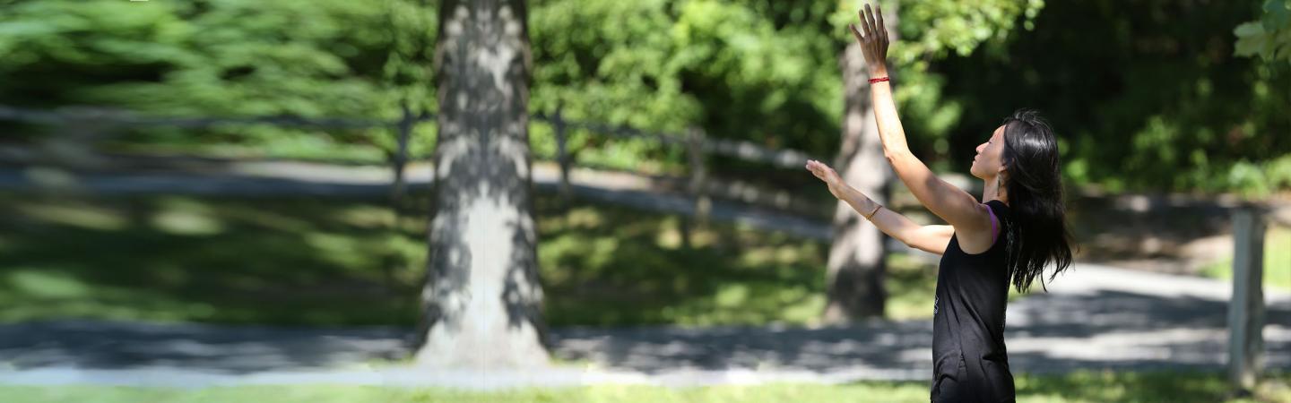 Woman practicing somatic movement outdoors in a peaceful, tree-lined setting, embodying mindfulness, body awareness, and holistic wellness through somatic healing practices.