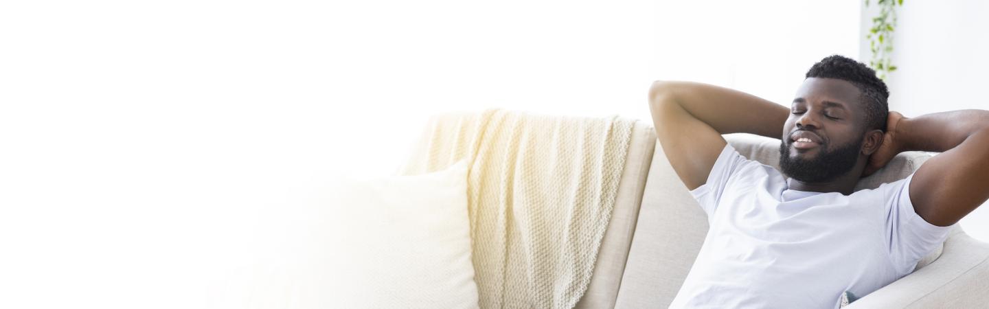 A relaxed man with closed eyes resting on a couch, illustrating calmness and relaxation as part of exercises to help you fall asleep with ease.