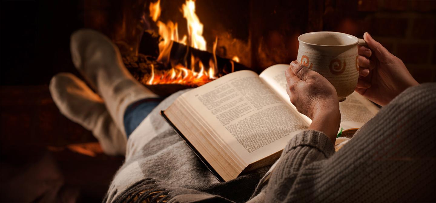 Reading by a warm fireplace with tea, evoking comfort and winter self-care.