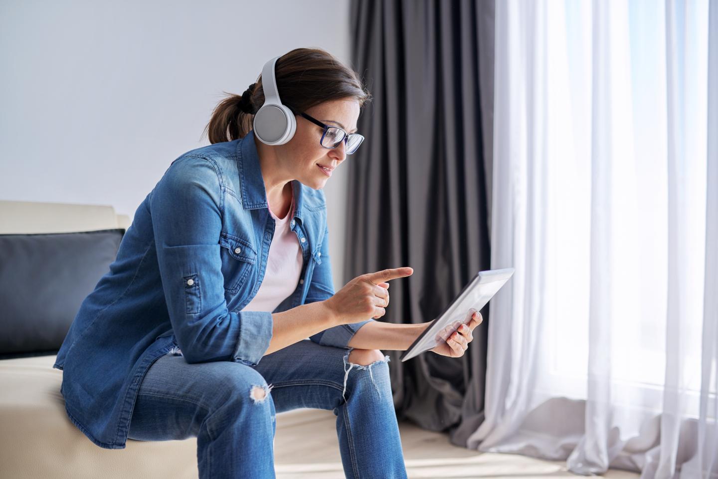 Woman wearing denim and headphones interacts with a tablet